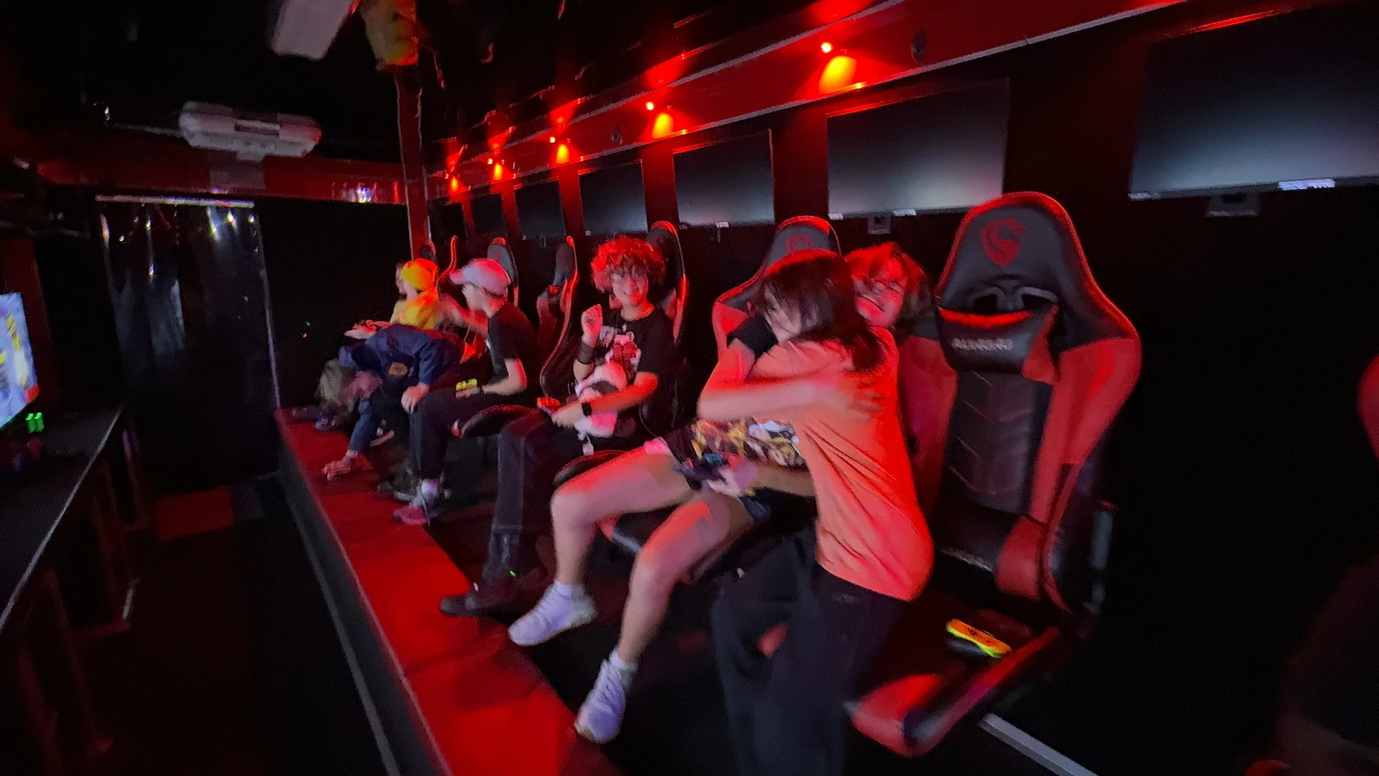 Players in gamer chairs under red lighting inside the theater