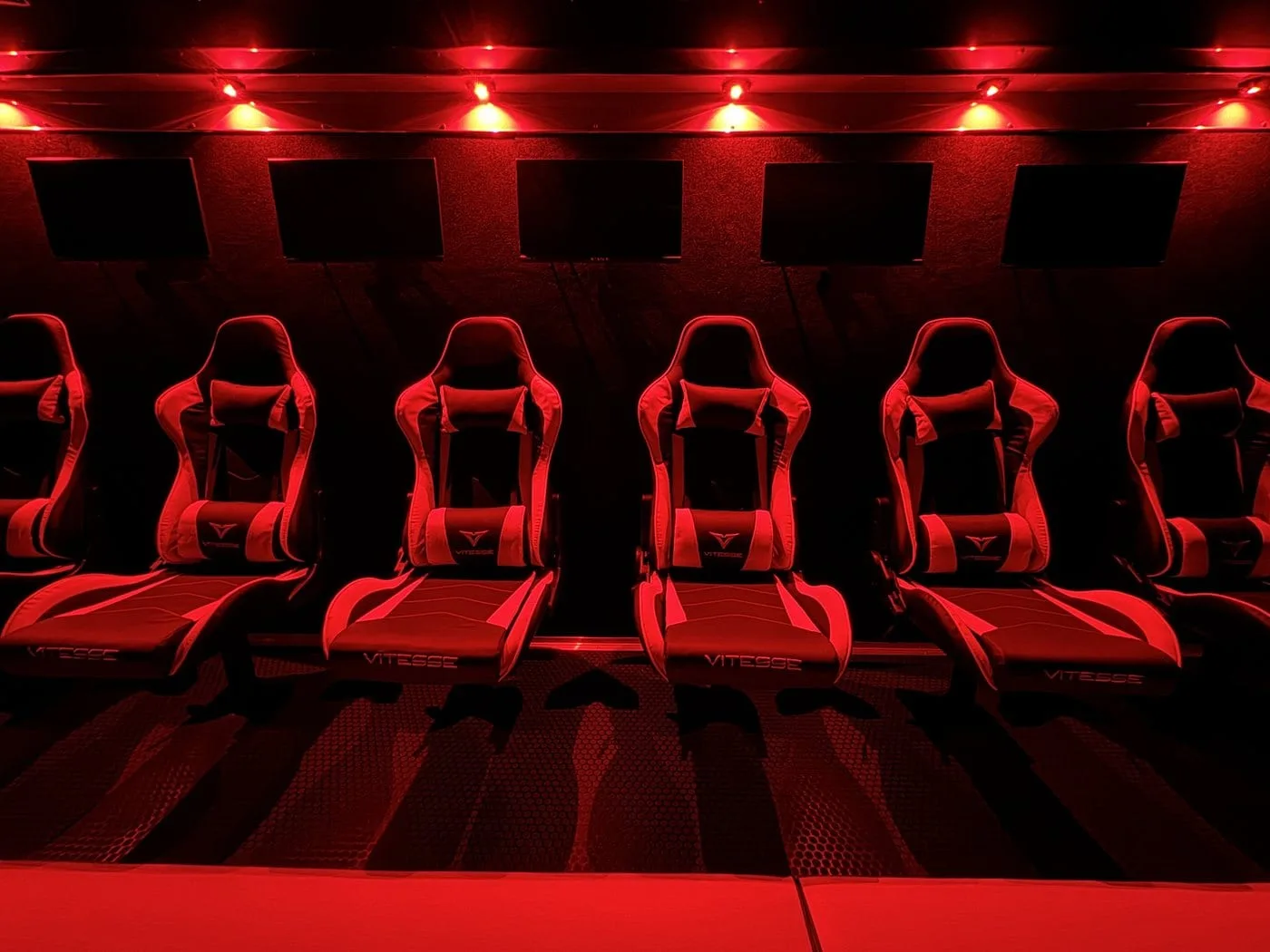Inside a Next Level Gaming theater with red LED lighting, game screens and luxury gamer chairs